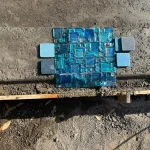 A blue mosaic tile on the ground beside a blue shoe, showcasing a vibrant color contrast.