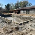 A construction site showing a backyard pool being built, with equipment visible around the site.