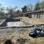 A construction site showing a backyard pool being built, with equipment visible around the site.