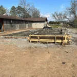 A construction site showing a backyard pool being built next to a house, with tools and materials visible.