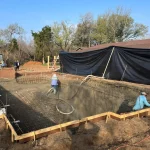 A construction site showing a backyard pool being built, with workers and equipment visible around the site.