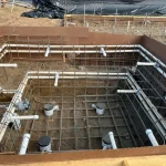 A construction site showing a backyard pool being built, with equipment visible around the site.