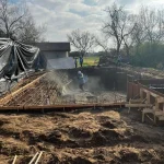 A construction site showing a backyard pool being built, with workers and equipment visible around the site.