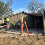 Construction workers in hard hats are actively building a house, using tools and materials on a residential site.