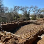 A construction site showing a backyard pool being built, with equipment visible around the site.