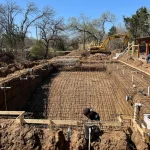 A construction site showing a backyard pool being built, with equipment visible around the site.