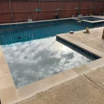 A swimming pool featuring a concrete edge and a surrounding stone wall, reflecting a serene outdoor environment.