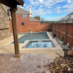 A swimming pool featuring a concrete edge and a surrounding stone wall, reflecting a serene outdoor environment.