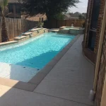A swimming pool featuring a concrete edge and a surrounding stone wall, reflecting a serene outdoor environment.