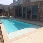 A swimming pool featuring a concrete edge and a surrounding stone wall, reflecting a serene outdoor environment.