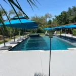 A serene pool scene featuring blue umbrellas and a blue tiled patio, creating a relaxing outdoor atmosphere.