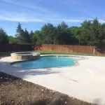 A backyard under construction featuring a pool surrounded by a wooden fence.