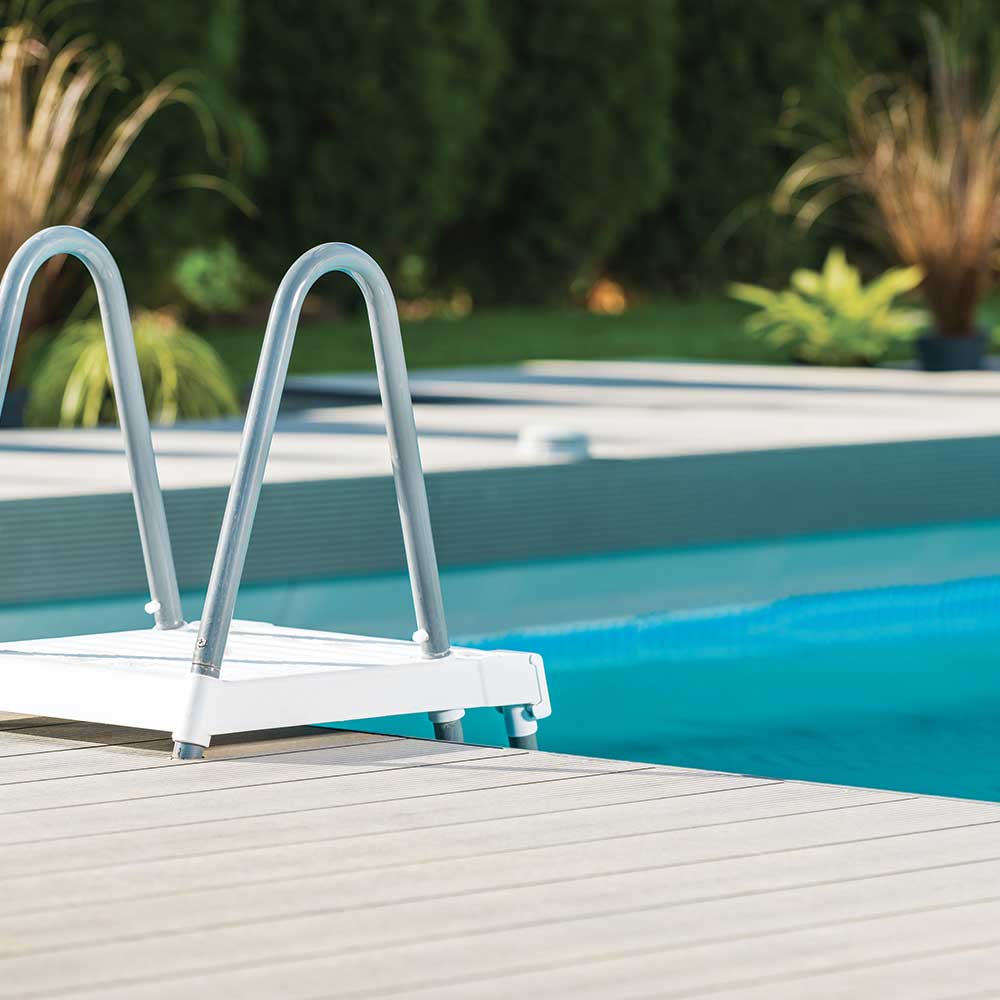 A white pool ladder rests on a wooden deck, ready for use by the swimming pool.