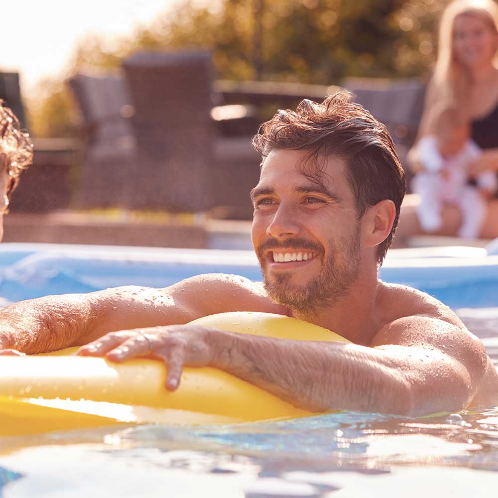 A handsome young man holds on to a yellow tube floating device.