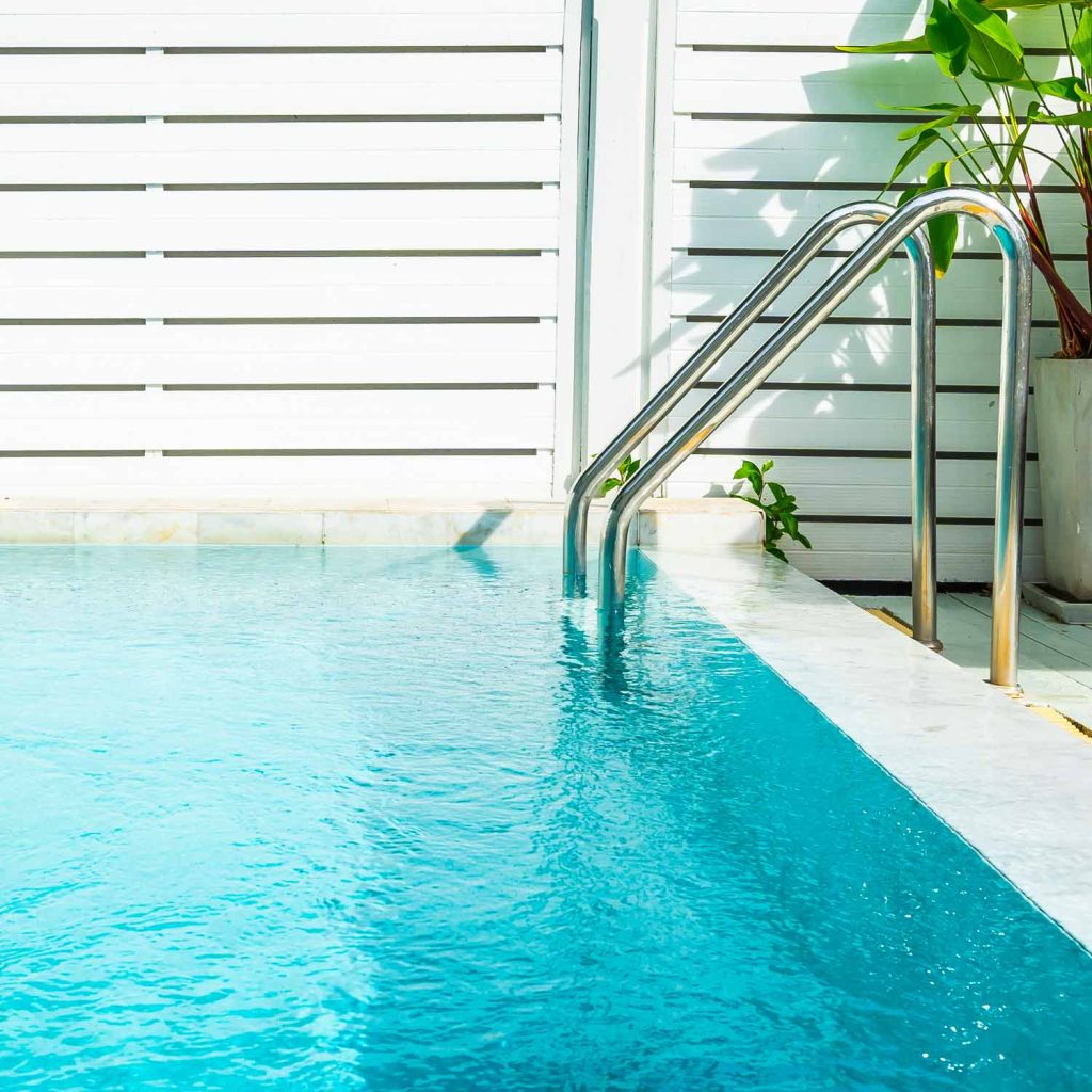 A white pool ladder rests on a wooden deck, ready for use by the swimming pool.