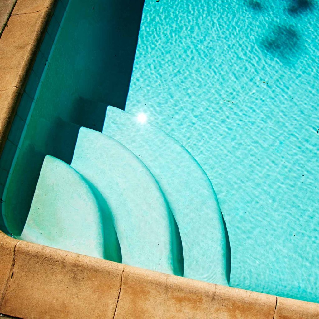 A clear blue swimming pool featuring a colorful surfboard resting on the edge.