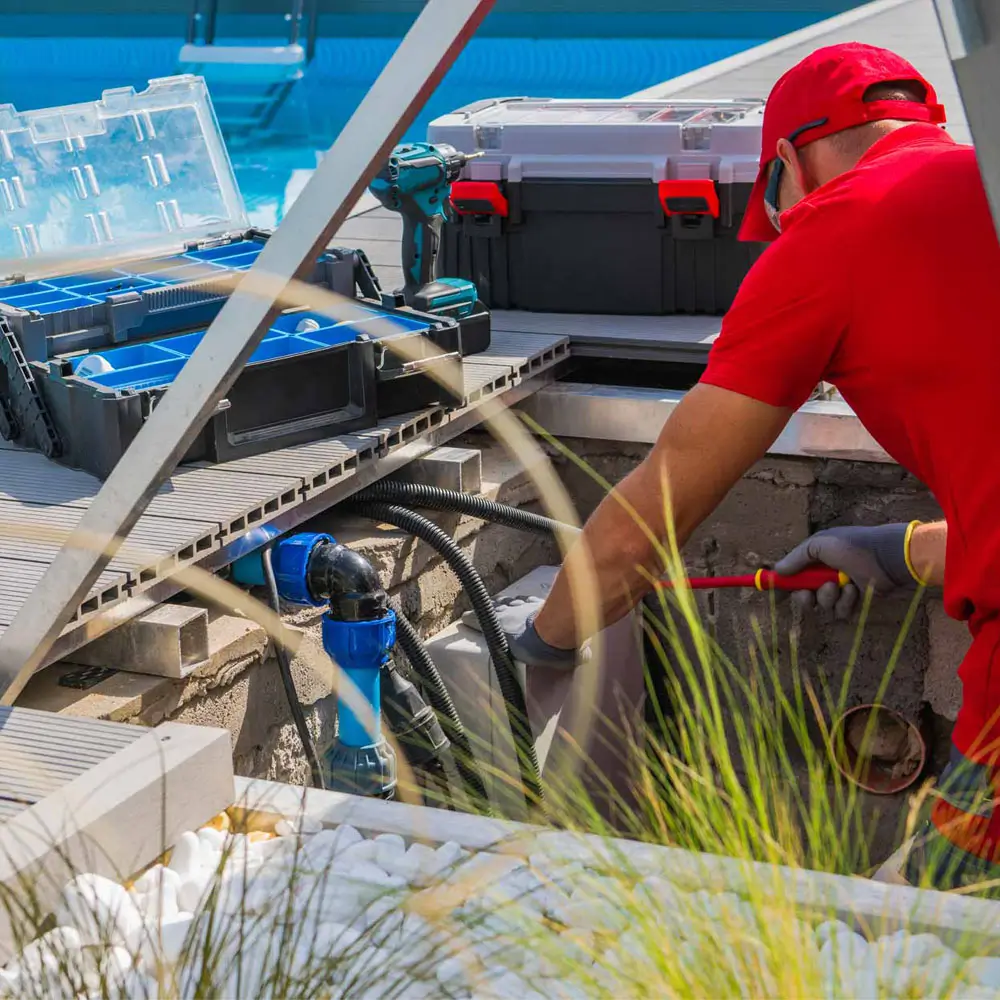 A man in a red shirt is cleaning and maintaining a swimming pool.